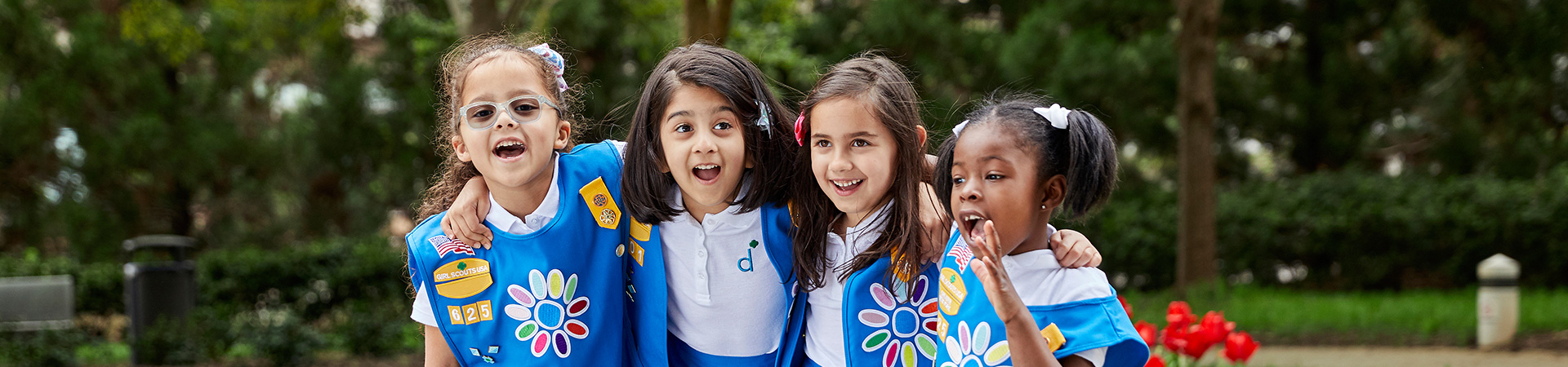  group of daisy girl scouts in vest and apron uniform hugging and smiling outside 